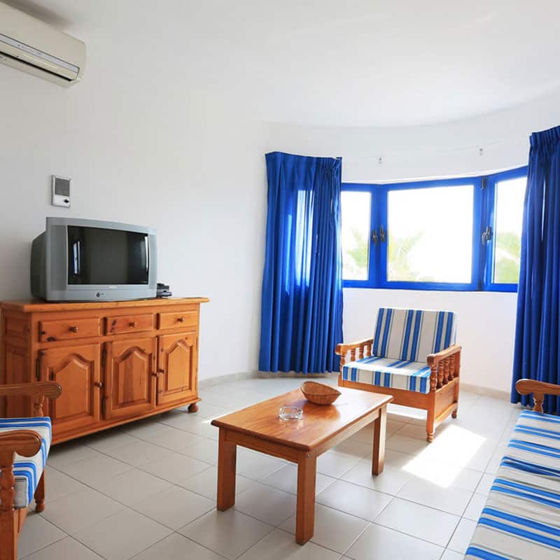aparthotel marromar con muebles de madera y television antigua con ventanas y cortinas azules